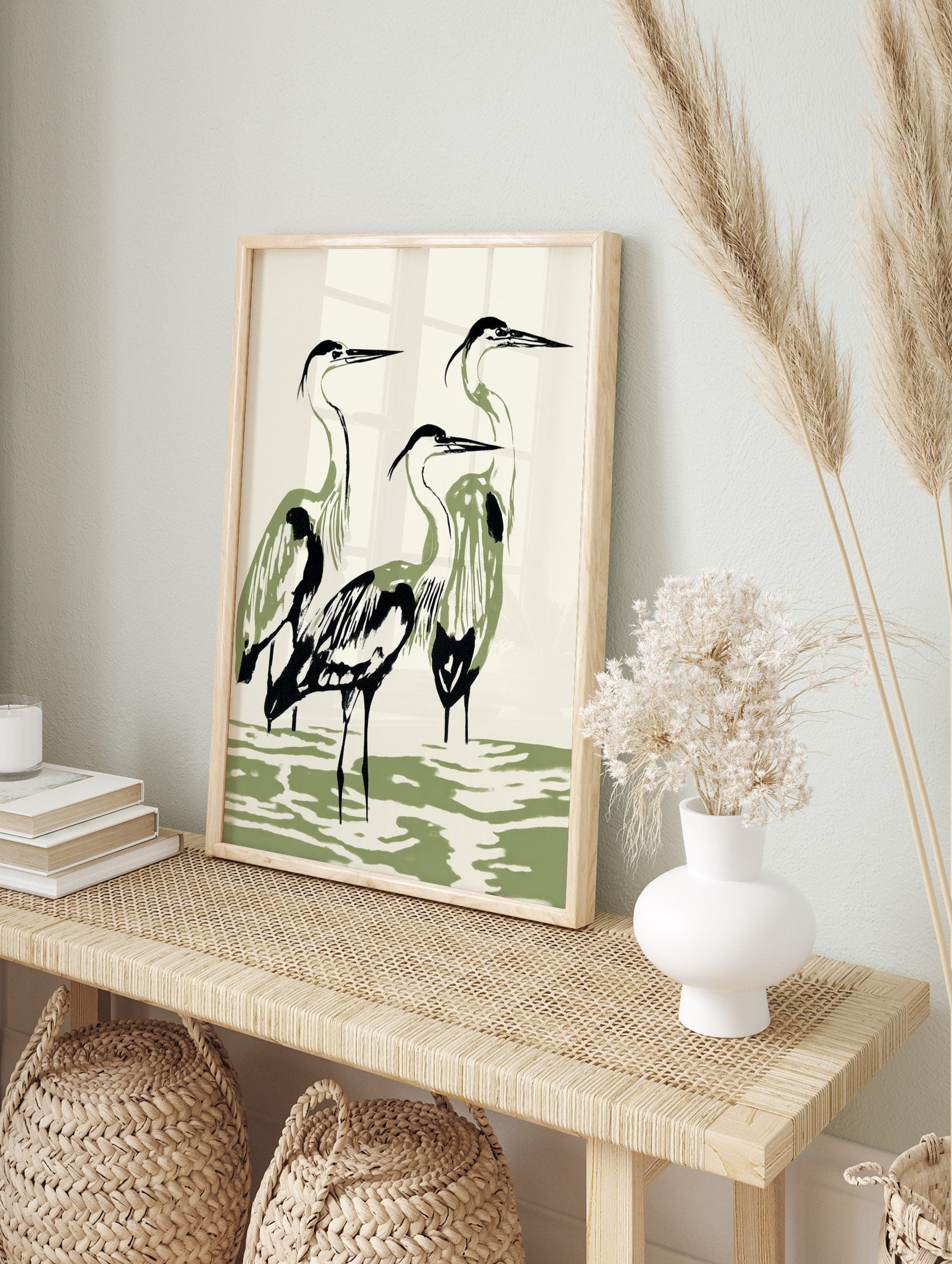 Minimalist illustration of three herons with black outlines and olive green bodies standing, in an alternate framed mockup