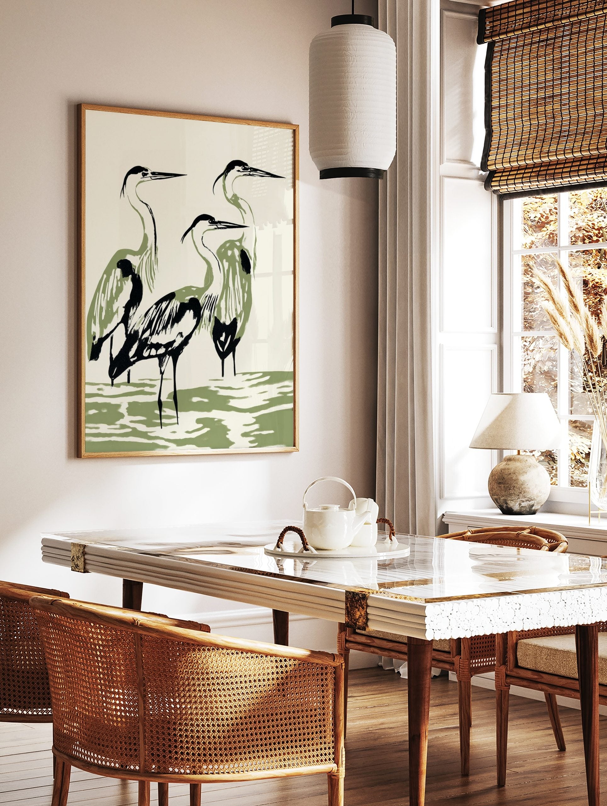 Minimalist illustration of three herons with black outlines and olive green bodies standing in water, in a styled room mockup