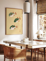 Three pufferfish in Japanese woodblock style with green bodies and orange fins on a cream background, in a styled room mockup