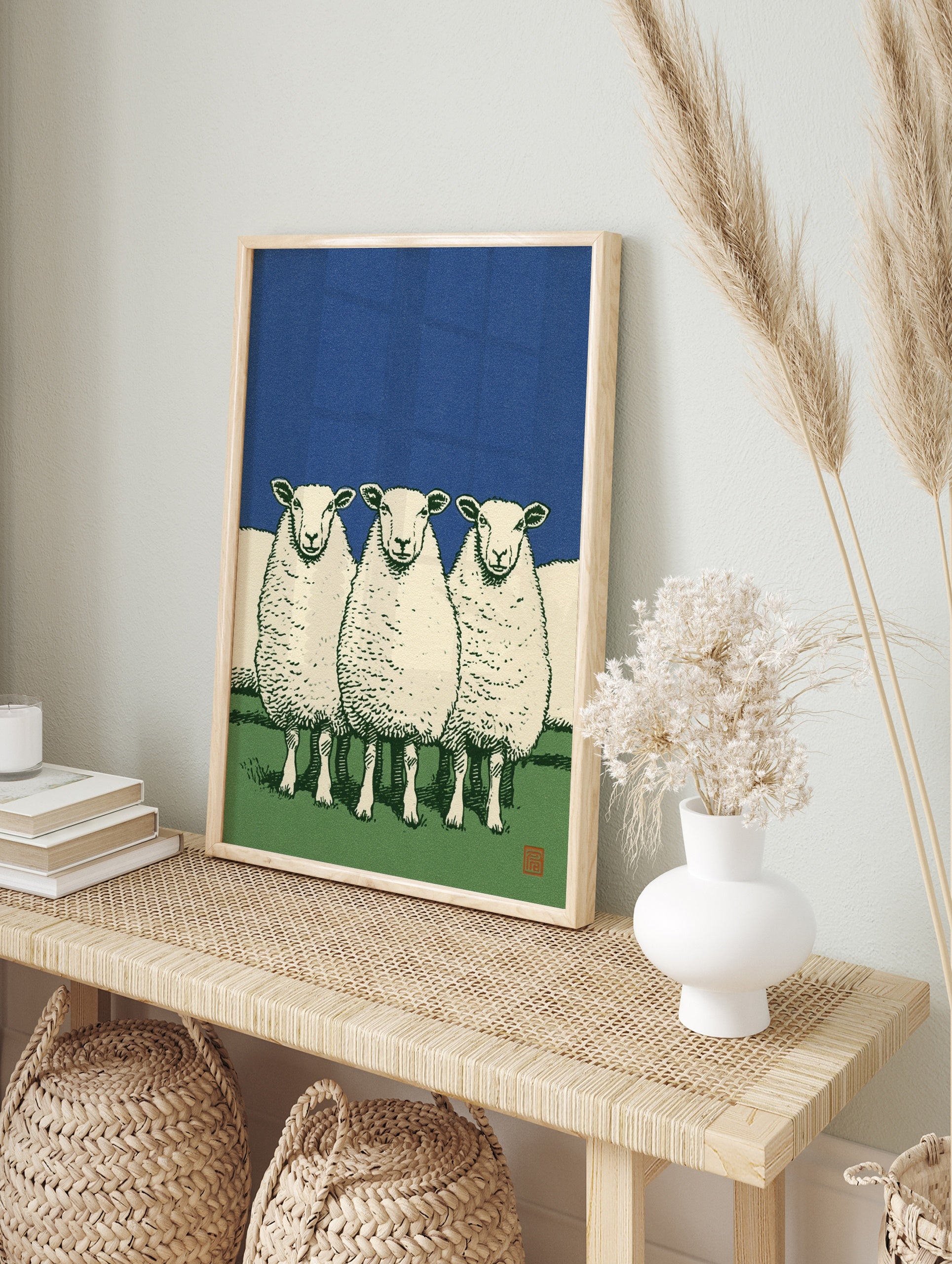 Illustrative art print of three white sheep standing in a green field against a solid deep, in an alternate framed mockup