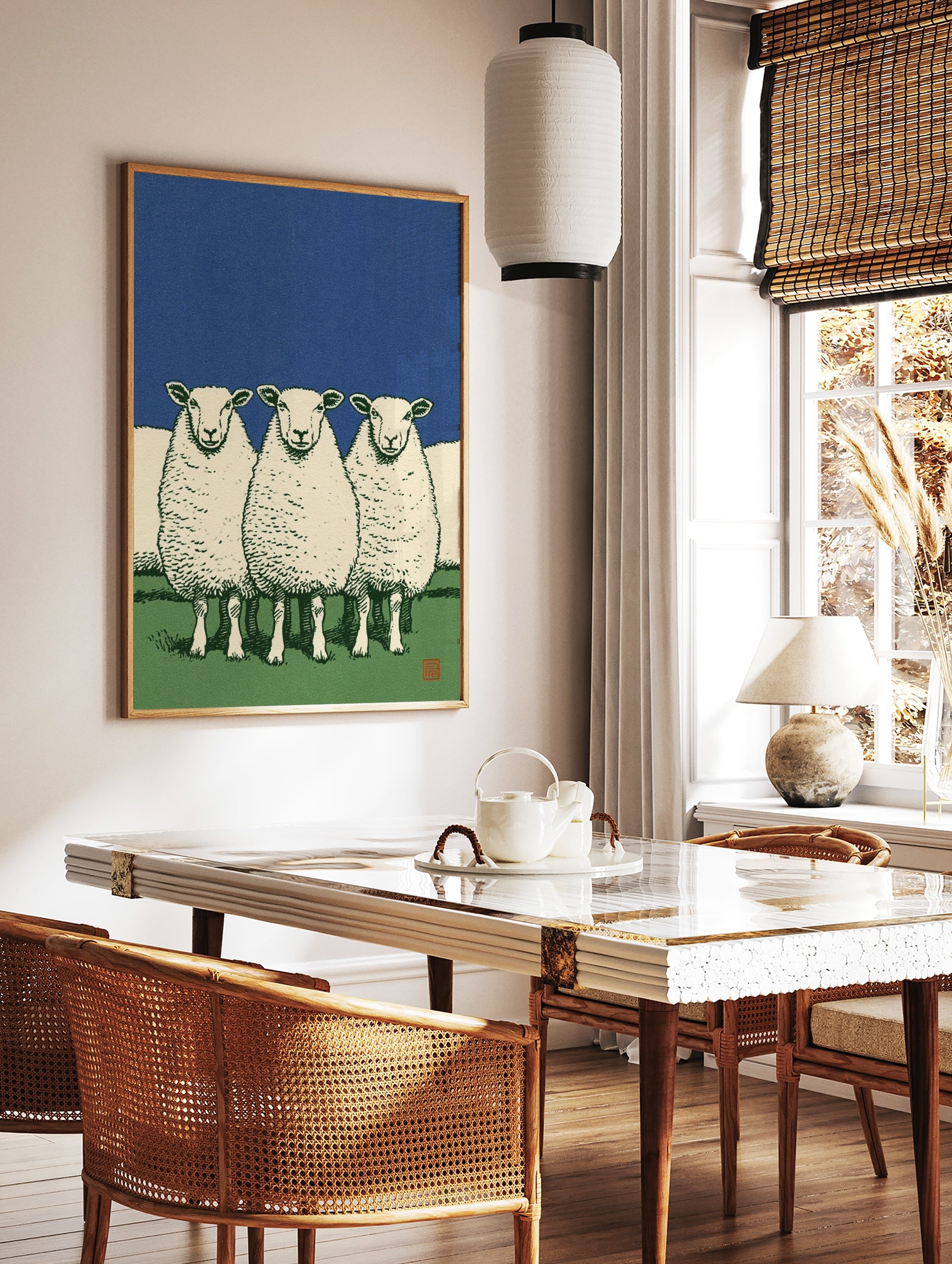 Illustrative art print of three white sheep standing in a green field against a solid deep blue sky, in a styled room mockup