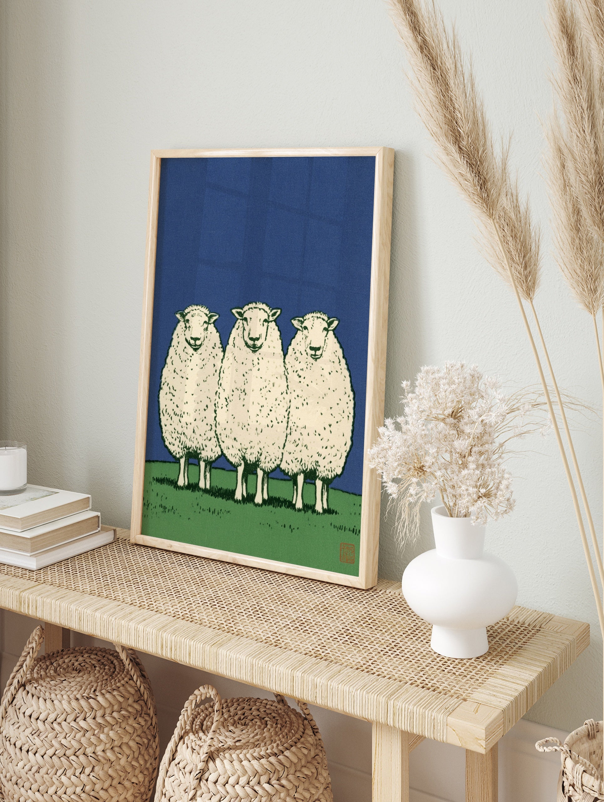 Three sheep standing in a row on a green field against a solid blue sky, illustrative art, in an alternate framed mockup