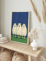 Three sheep standing in a row on a green field against a solid blue sky, illustrative art, in an alternate framed mockup