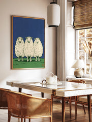 Three sheep standing in a row on a green field against a solid blue sky, illustrative art print, in a styled room mockup