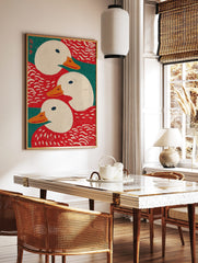 Illustrative art print showing three white ducks with orange beaks against red and teal green, in a styled room mockup