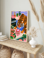A whimsical illustration of a tiger icing a strawberry cake in a colourful kitchen with blue, in an alternate framed mockup