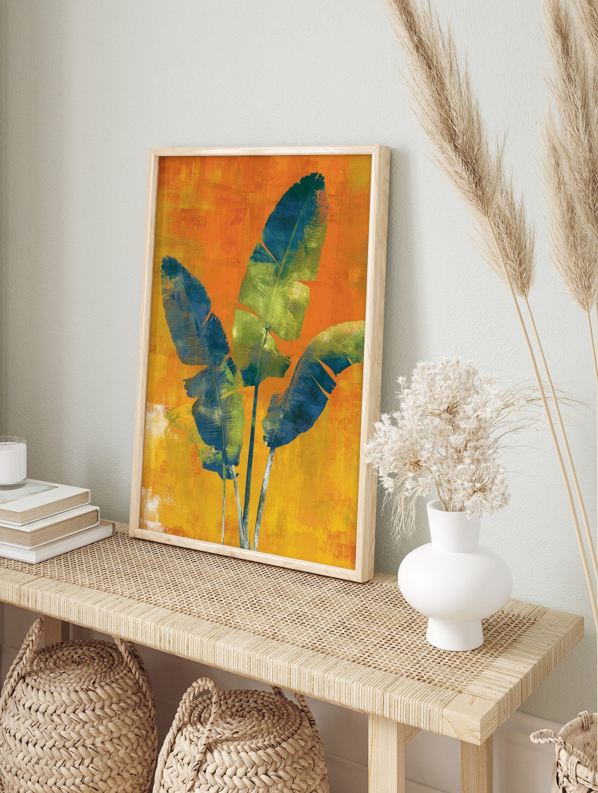 Three large blue and green tropical leaves on a textured orange and yellow background wall, in an alternate framed mockup