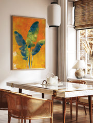 Three large blue and green tropical leaves on a textured orange and yellow background wall art print, in a styled room mockup
