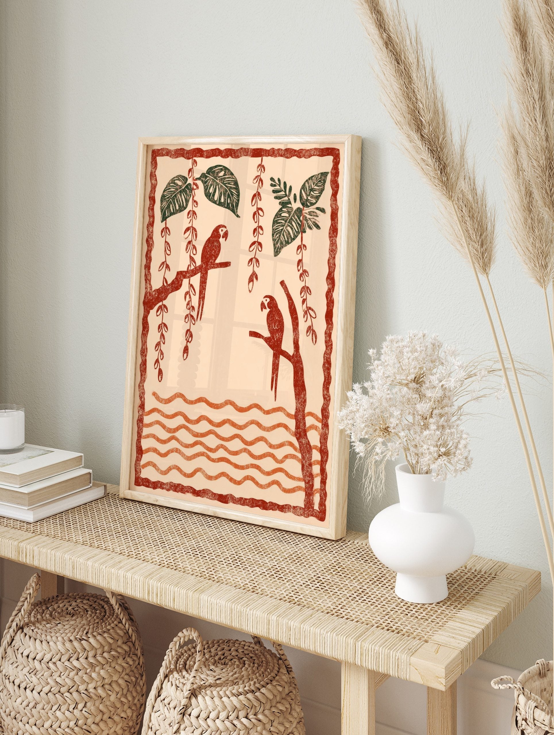 Illustrative art print of two red parrots on branches with green tropical leaves and orange, in an alternate framed mockup
