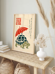 Illustrative print of a turtle with a red umbrella, Japanese script, and red seal on a cream, in an alternate framed mockup