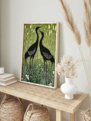 Two black cranes standing in a green and white wetland with tall reeds and cattails, in, in an alternate framed mockup