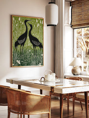 Two black cranes standing in a green and white wetland with tall reeds and cattails, in linocut, in a styled room mockup