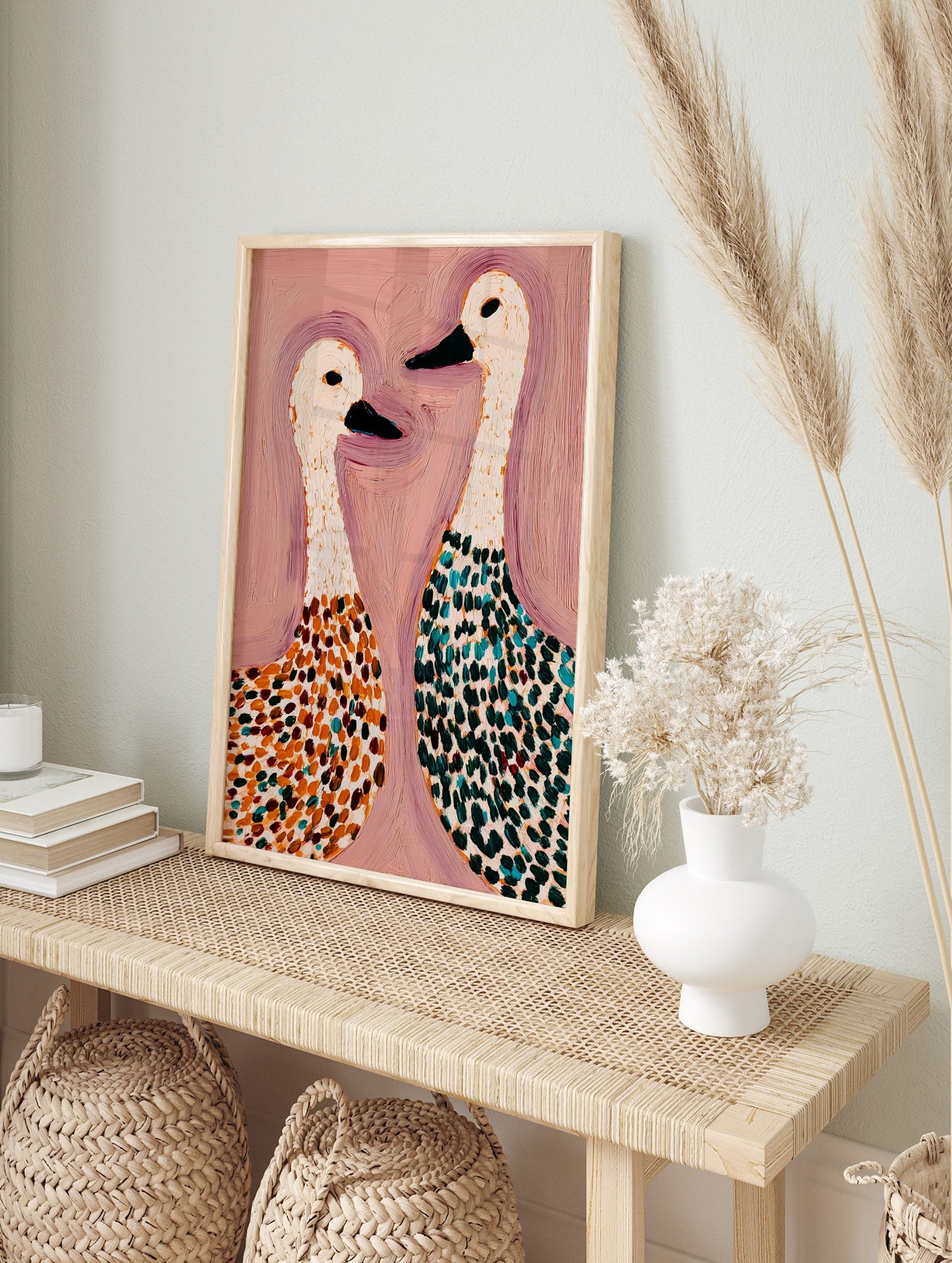 Abstract painting of two white geese with spotted bodies in orange, teal, and green on a pink, in an alternate framed mockup