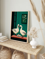 Two white geese with red beaks facing each other over cake slices on a table, against a teal, in an alternate framed mockup