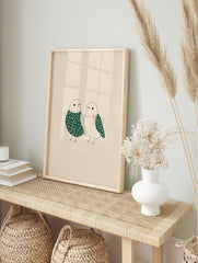 Illustrative art print of two birds with green and beige floral patterns on a light background, in an alternate framed mockup