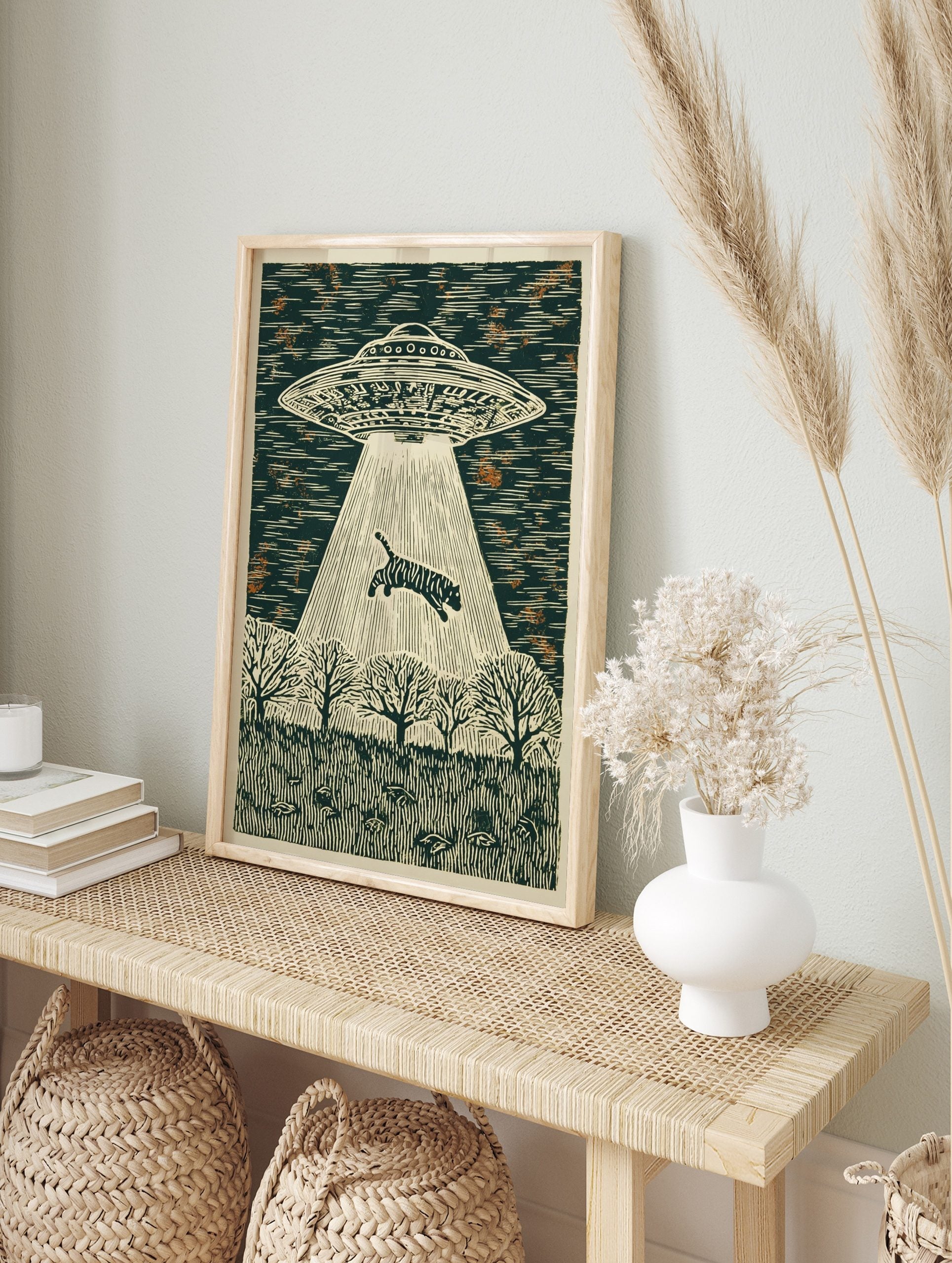Illustrative woodcut style print of a UFO abducting a striped tiger with a light beam over a, in an alternate framed mockup