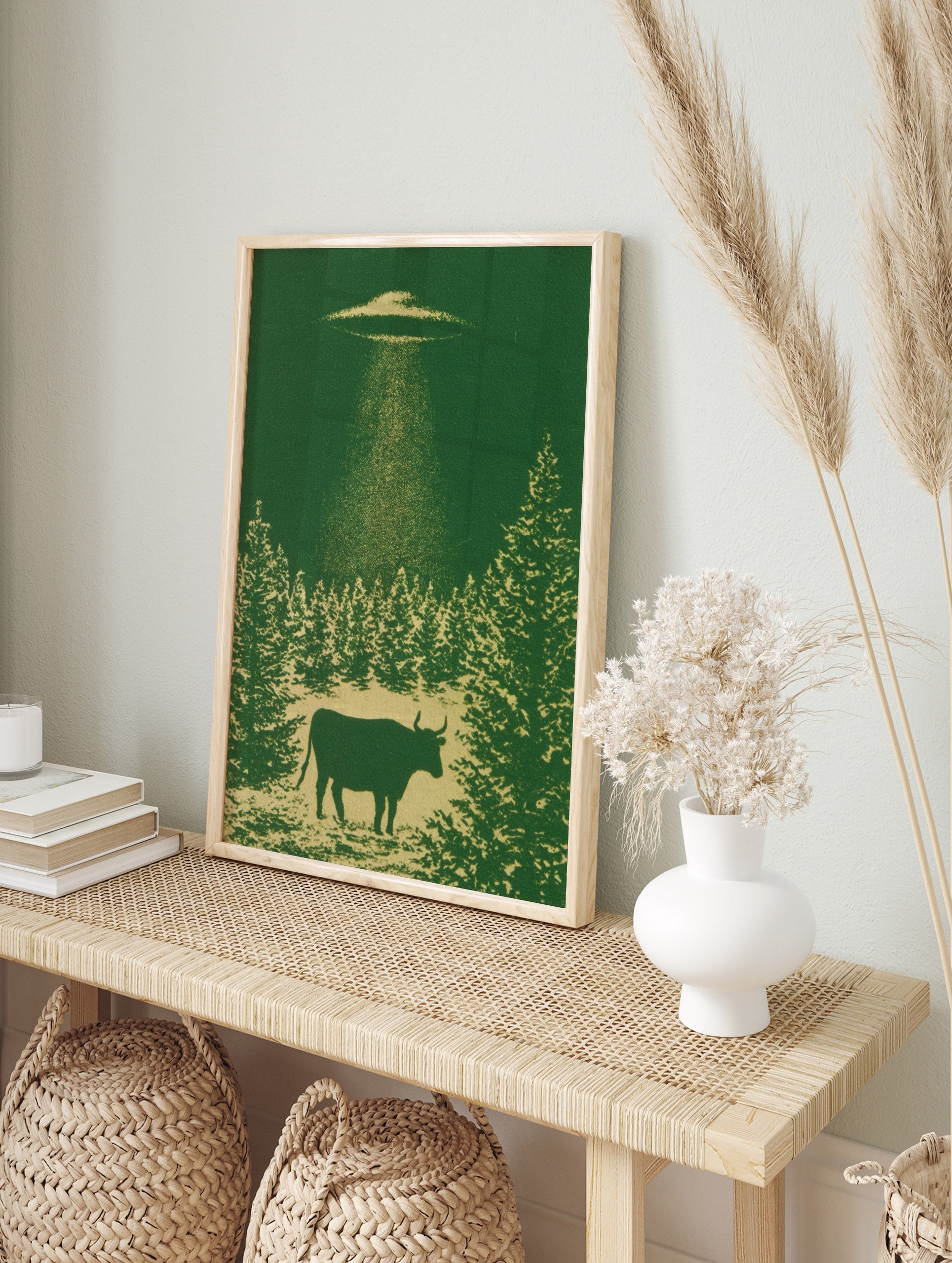 Monochromatic green wall art print of a cow being abducted by a UFO above a forest silhouette, in an alternate framed mockup