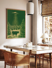 Monochromatic green wall art print of a cow being abducted by a UFO above a forest silhouette, in a styled room mockup