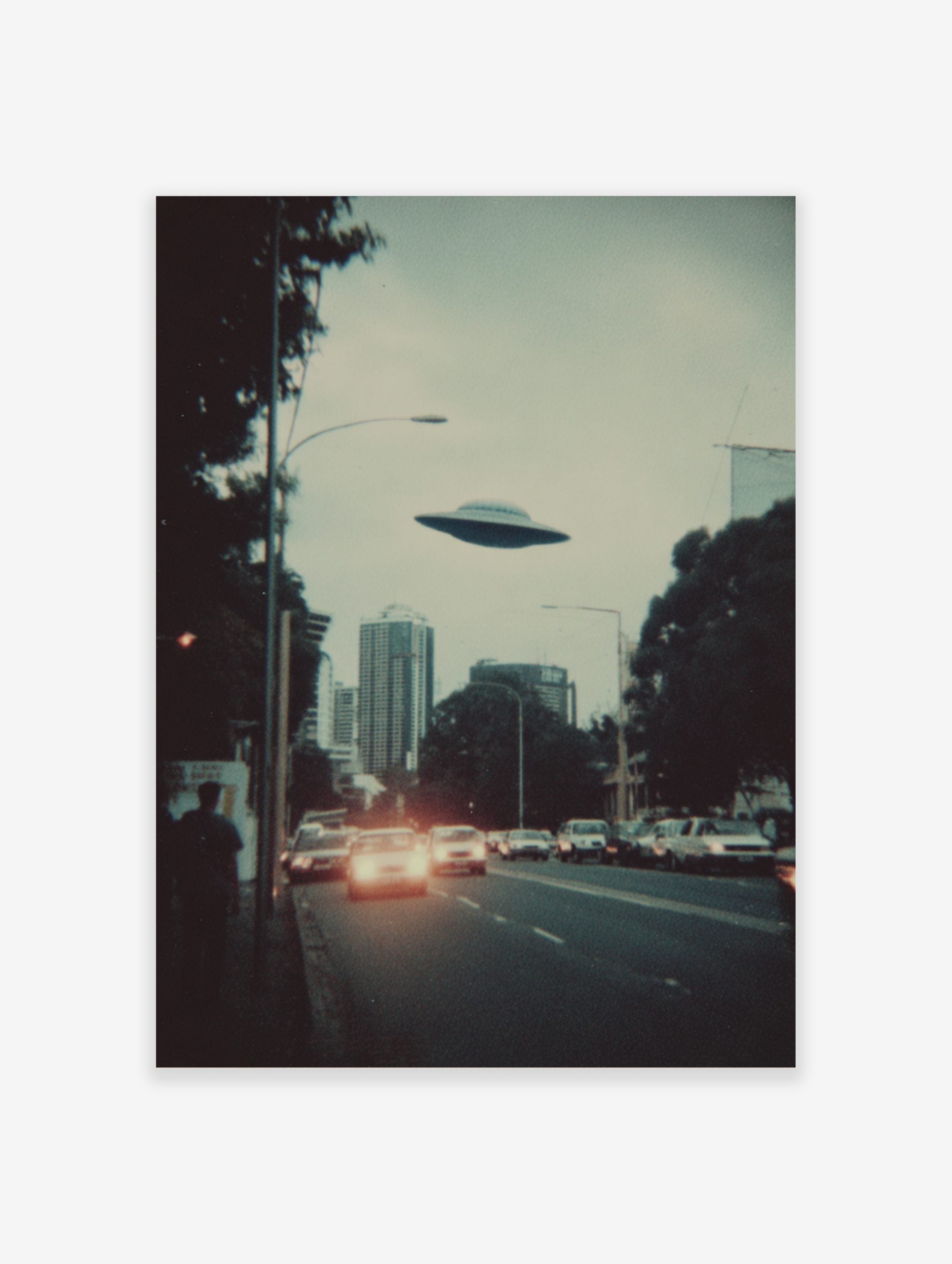 Retro sci-fi print of a UFO flying over a city skyline with cars and buildings at dusk