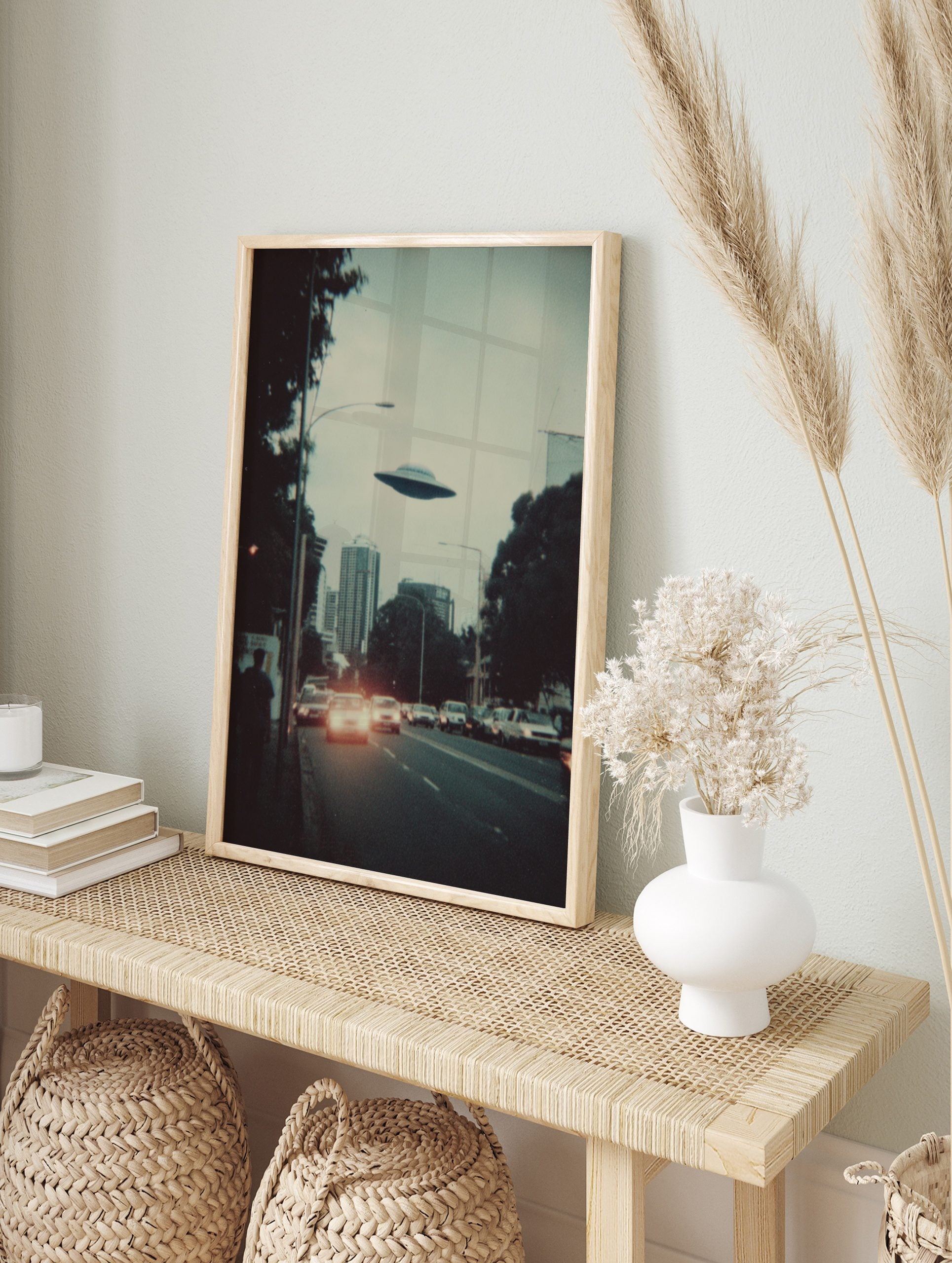 Retro sci-fi print of a UFO flying over a city skyline with cars and buildings at dusk, in an alternate framed mockup