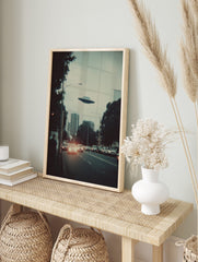Retro sci-fi print of a UFO flying over a city skyline with cars and buildings at dusk, in an alternate framed mockup