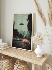 Photographic print of a dark disc-shaped UFO hovering over a city street with cars and, in an alternate framed mockup