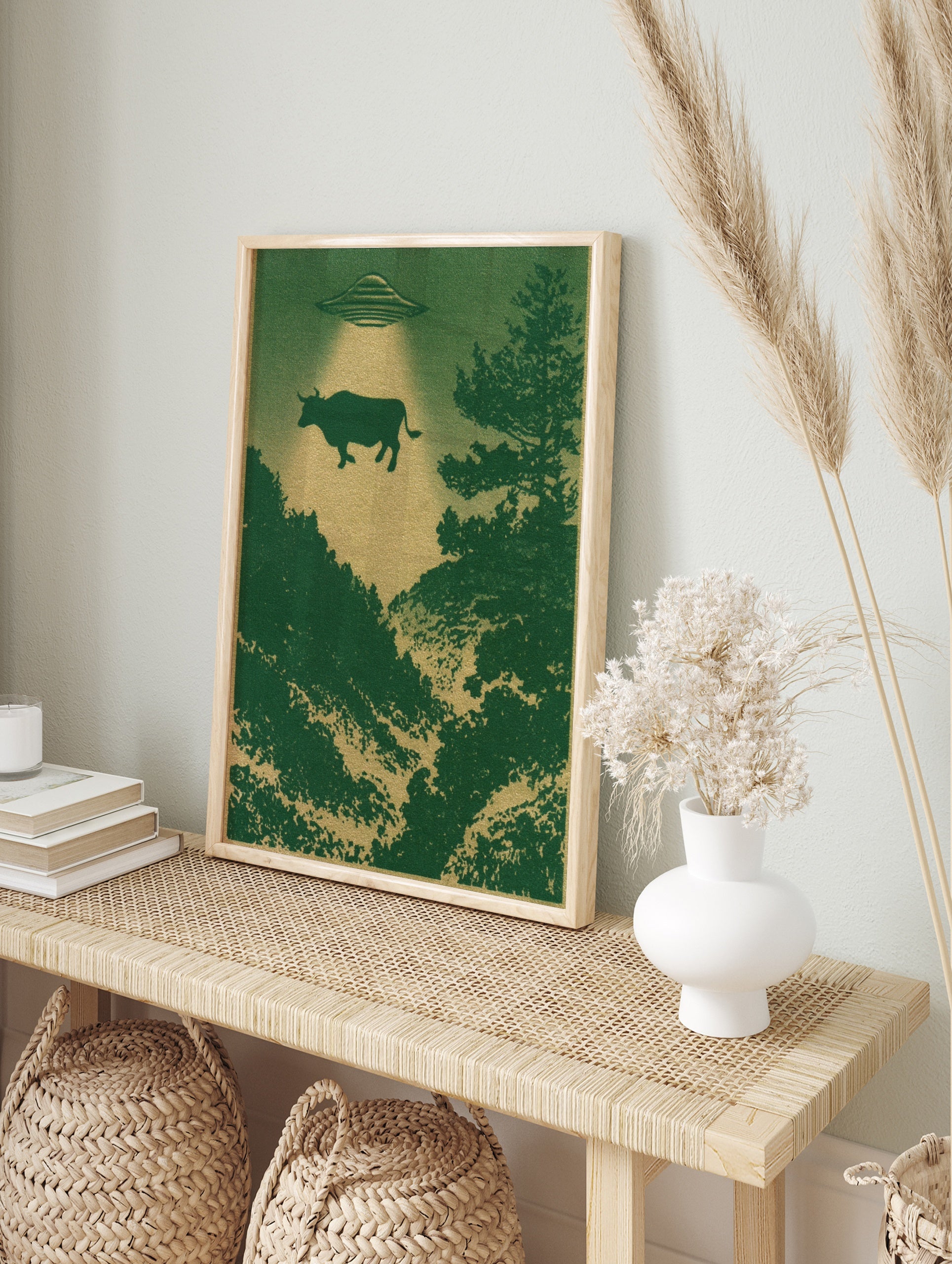 Surreal UFO abduction scene with a cow floating above a dark green forest, illustrated poster, in an alternate framed mockup