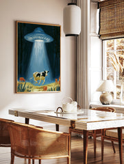 Surreal illustrative art print of a UFO abducting a cow with a glowing light beam in a dark forest, in a styled room mockup