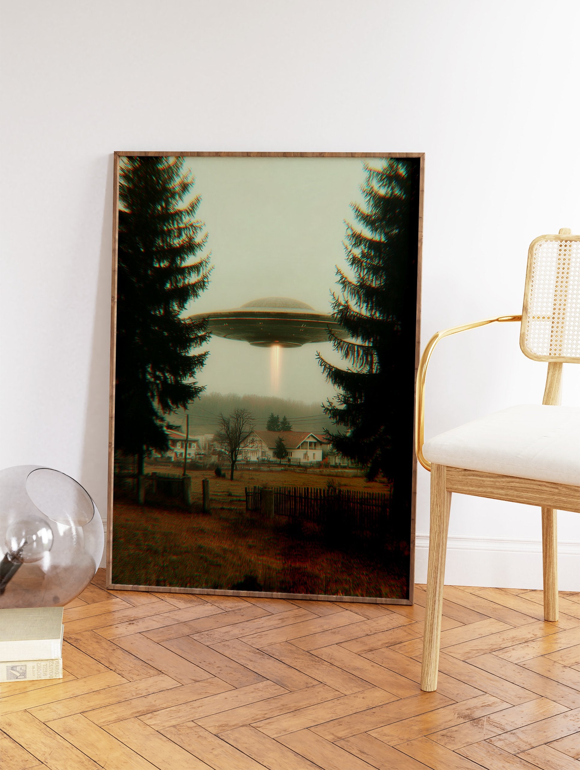 UFO flying saucer with a light beam hovers over a misty village framed by two dark evergreen trees. Mysterious sci-fi wall art. - Image 2