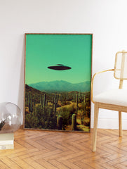 UFO flying saucer hovering over a desert landscape with saguaro cacti and mountains under a teal sky, surreal wall art. - Image 2