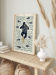 Illustrative print of a navy blue scuba diver with olive flippers swimming among fish and, in an alternate framed mockup