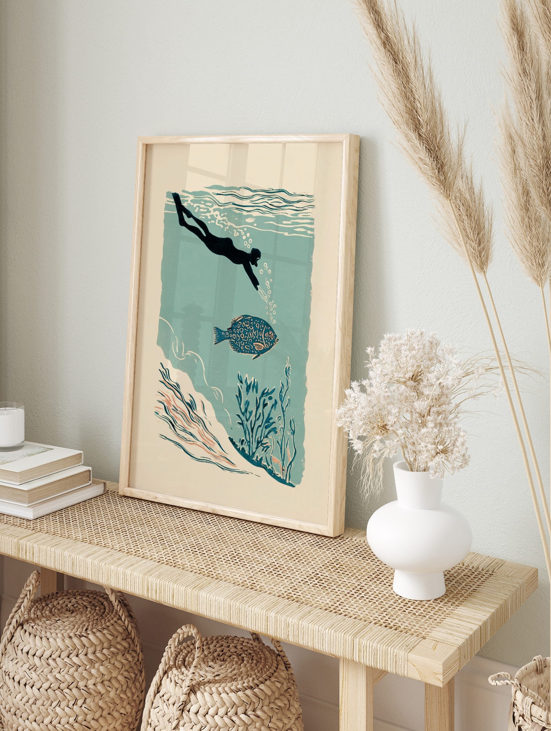 Illustrative print of a diver swimming with a patterned blue fish in teal water with, in an alternate framed mockup