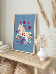 Cream unicorn with red horn and mane prancing among red stars on a light blue background, in an alternate framed mockup