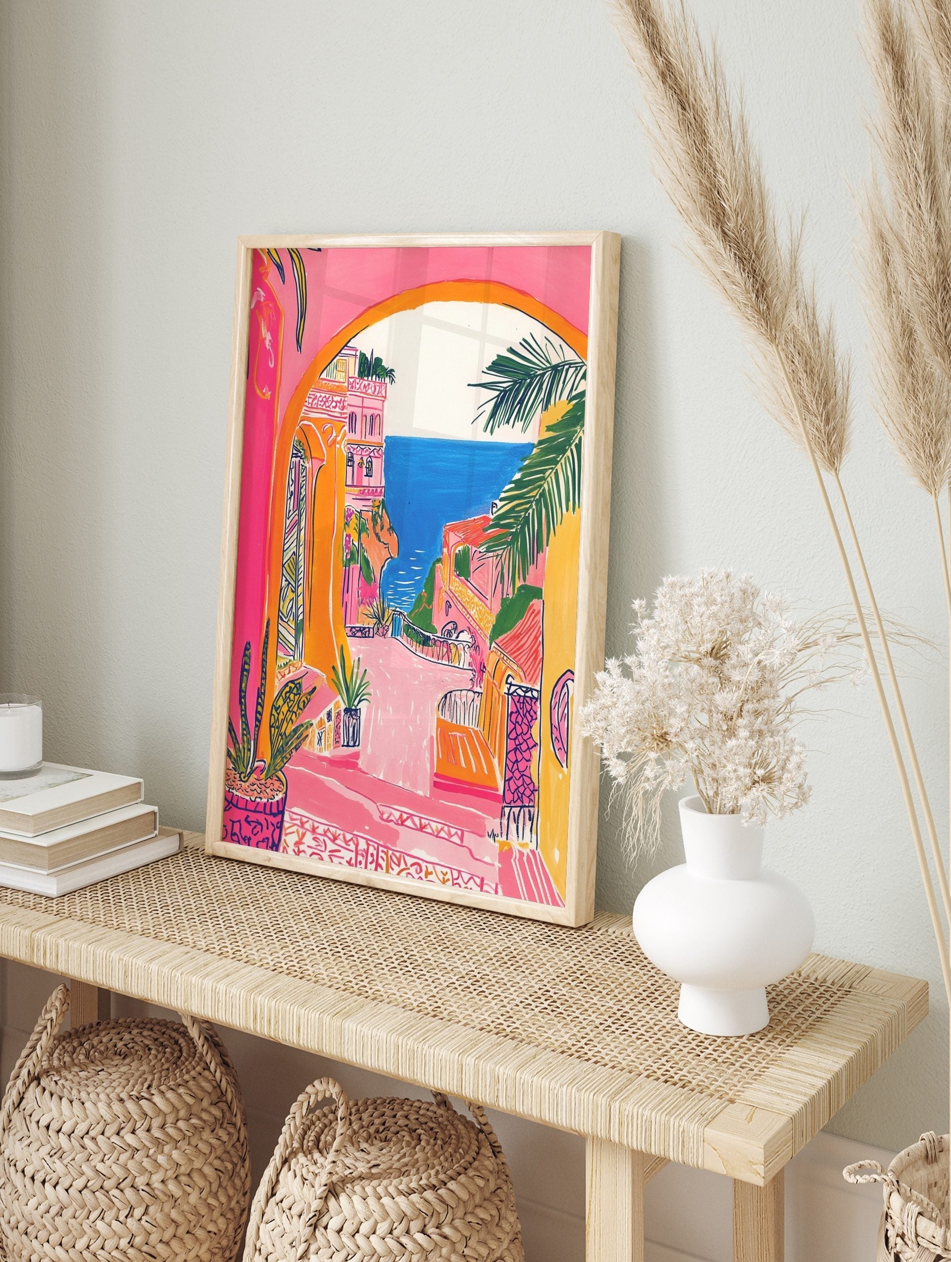 Vibrant illustrative print of a coastal town through an archway, featuring pink buildings, in an alternate framed mockup