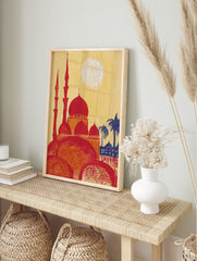 Illustrative print of a red mosque with multiple domes and minarets, yellow sky, blue palm, in an alternate framed mockup