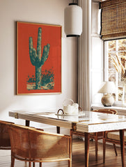 Illustrative Saguaro cactus print in dark teal and beige against a vibrant reddish-orange, in a styled room mockup