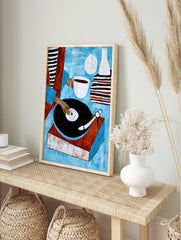 Illustrative art print of a person using a vinyl record player with a coffee cup and stacked, in an alternate framed mockup