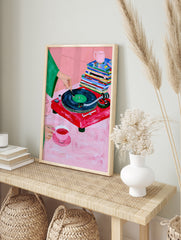 Illustrative art print of a red vinyl record player, tea set, and magazines on a pink, in an alternate framed mockup