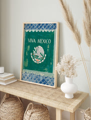 VIVA MEXICO wall art with white text and Mexican eagle emblem on dark green, framed by blue, in an alternate framed mockup