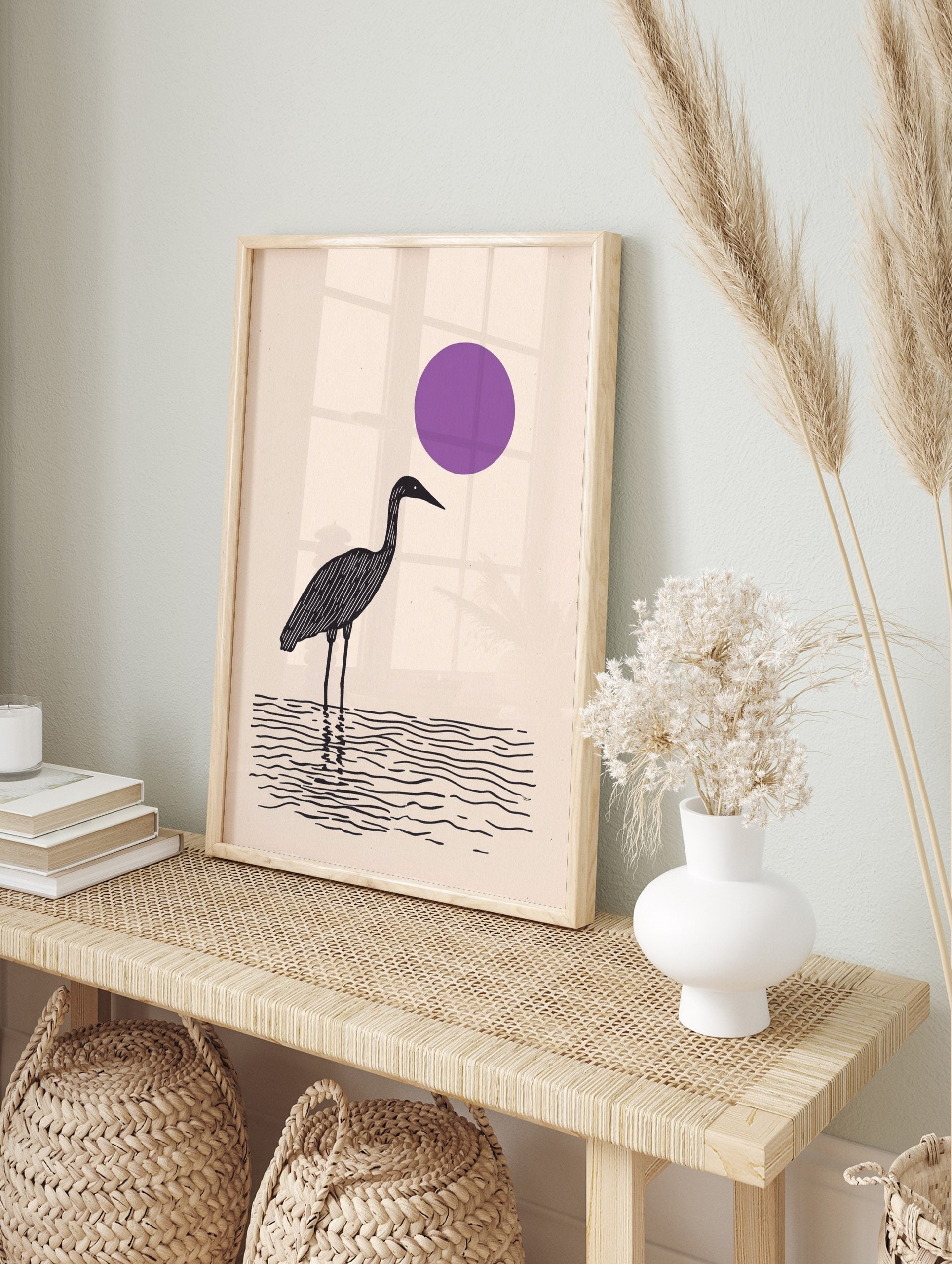 Minimalist black wading bird standing in water with a large purple sun on a beige background, in an alternate framed mockup