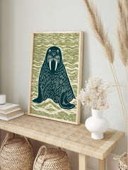 Linocut style walrus illustration with large tusks, dark teal on wavy green background, in an alternate framed mockup
