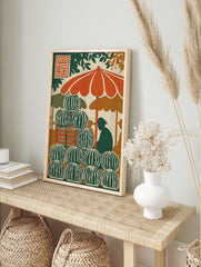 Illustrative print of a watermelon stand with stacked fruit, orange umbrella, and vendor, in an alternate framed mockup
