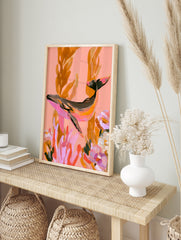 Painterly whale illustration swimming among seaweed and flowers in pink and orange tones, in an alternate framed mockup