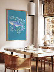 Illustrative blue whale art print with pink, yellow, and white seaweed on a teal background, in a styled room mockup