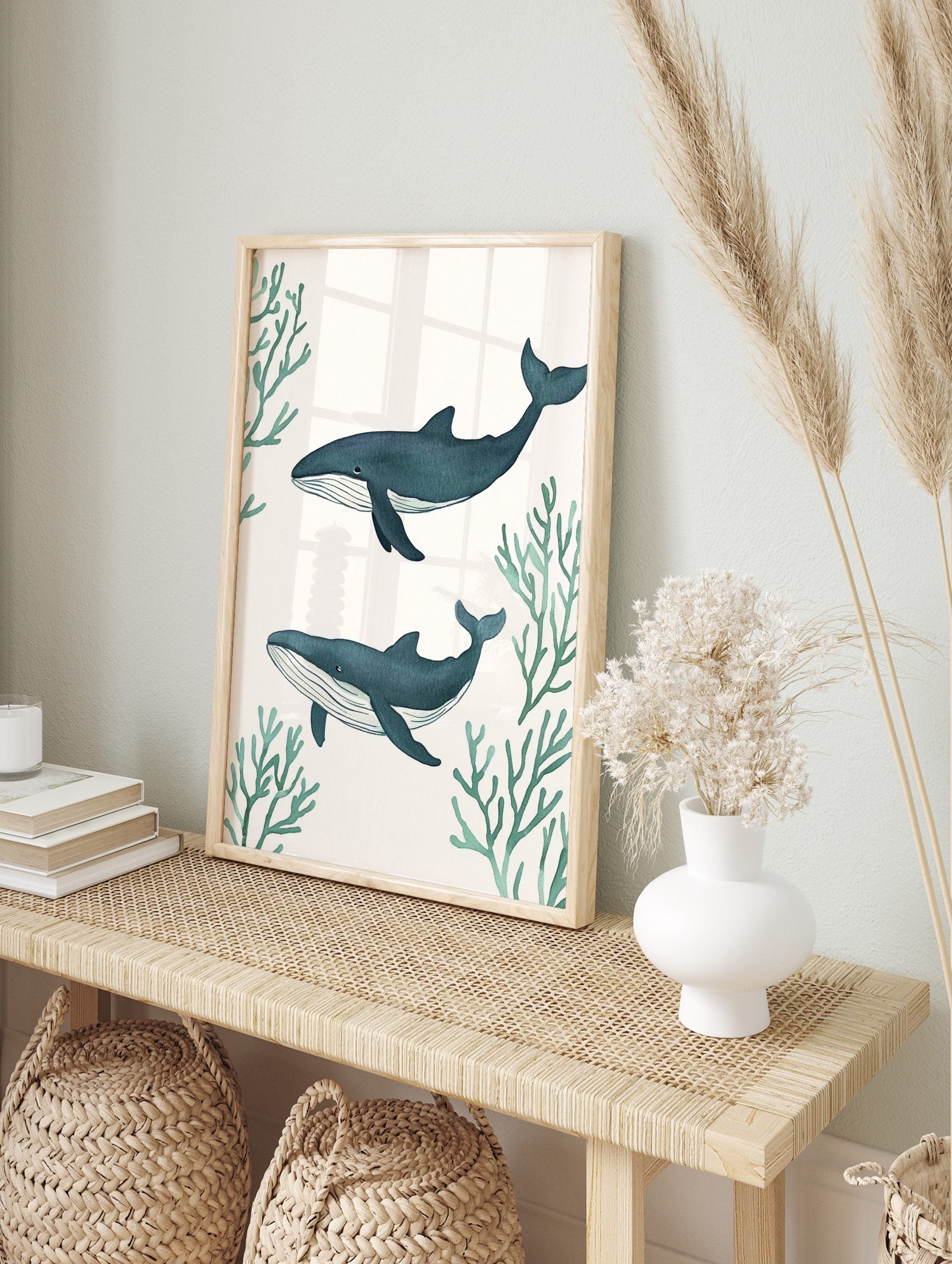 Two illustrative blue whales swimming horizontally amidst green coral branches on a white, in an alternate framed mockup