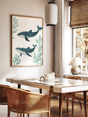 Two illustrative blue whales swimming horizontally amidst green coral branches on a white background, in a styled room mockup