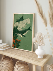 Spotted whale swimming amongst white coral and orange flowers on a green background, in an alternate framed mockup