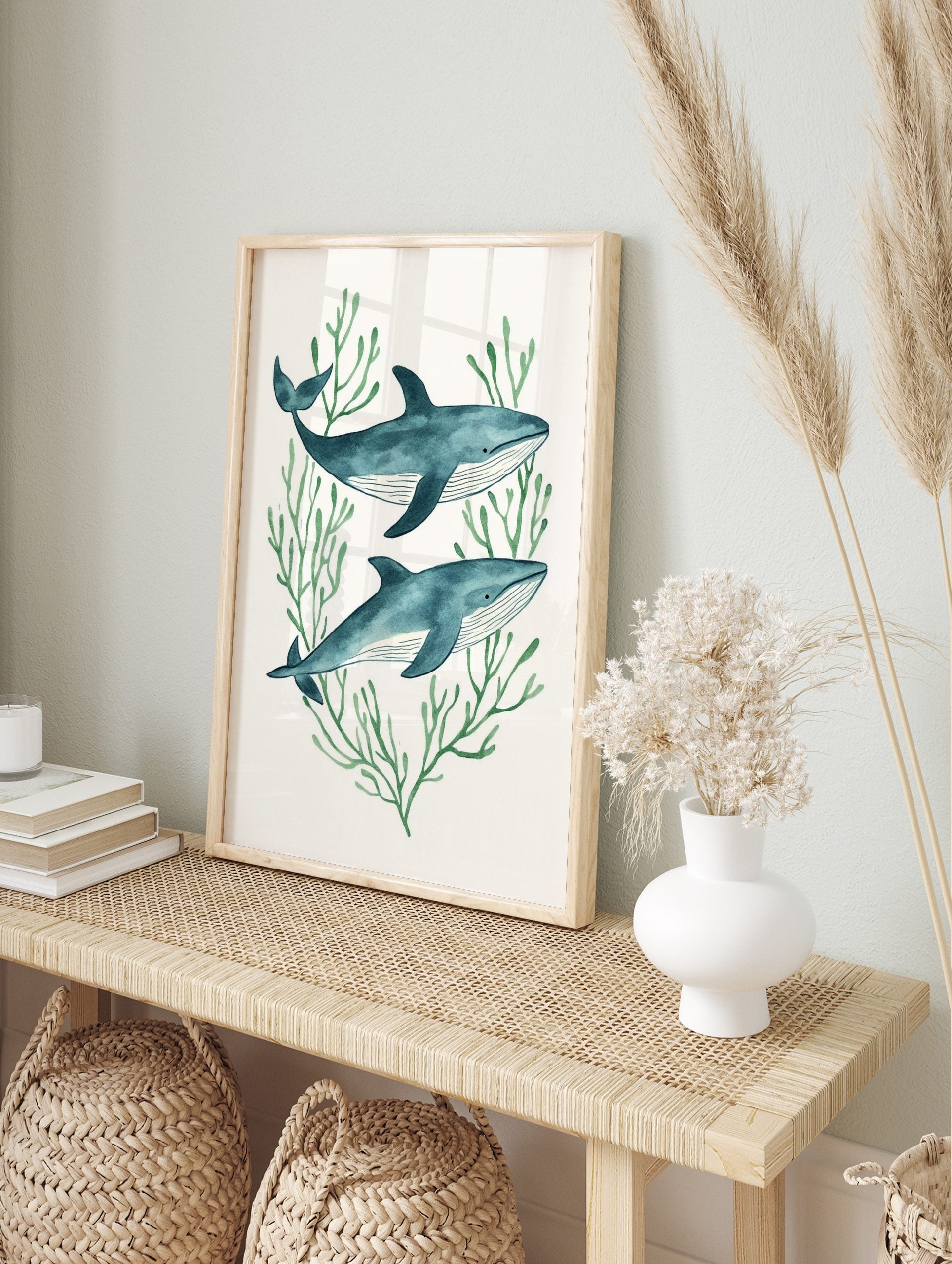 Illustrative watercolor print of two blue whales swimming among green seaweed on a white, in an alternate framed mockup