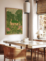 Illustrative print of a whimsical cottage with green roof, surrounded by lush green trees and, in a styled room mockup