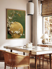 White cherry blossom branches curving over a golden full moon against a deep green background, in a styled room mockup
